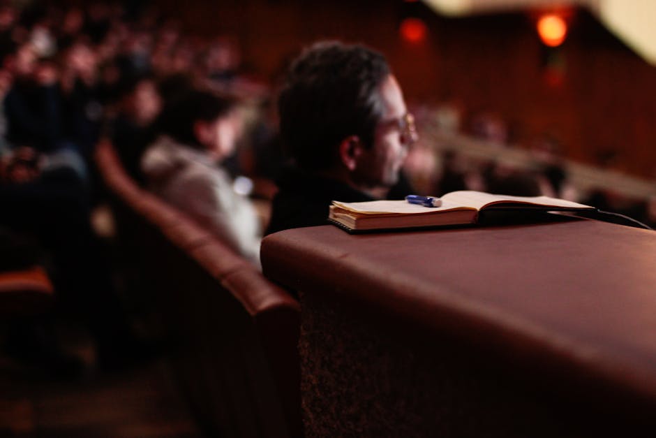 A focused shot of a notebook and pen in an auditorium with blurred audience.